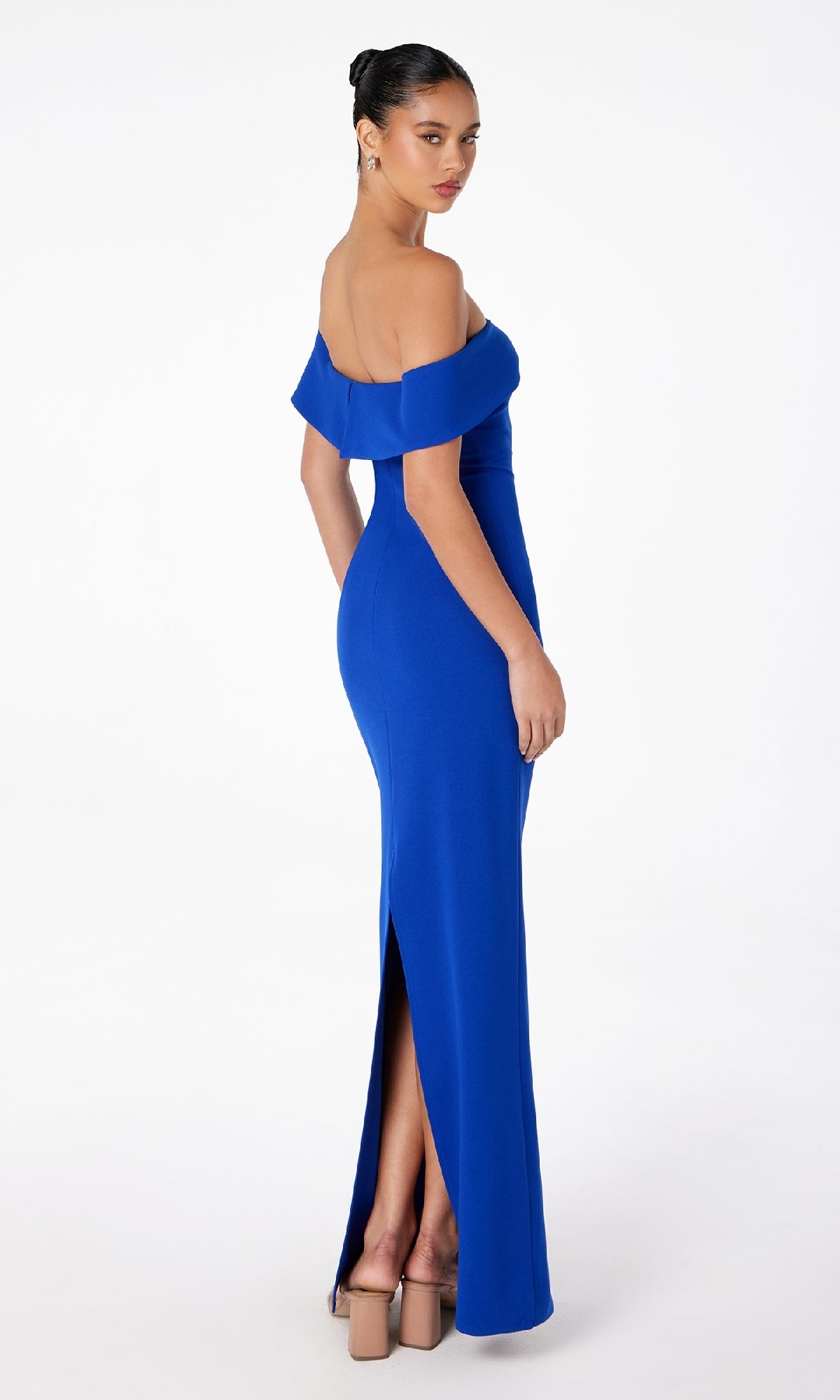 A woman stands on a white background wearing the Astee T2011 Off-the-Shoulder Long Prom Dress in royal blue with a floor-length silhouette, back slit, and nude high-heeled sandals.